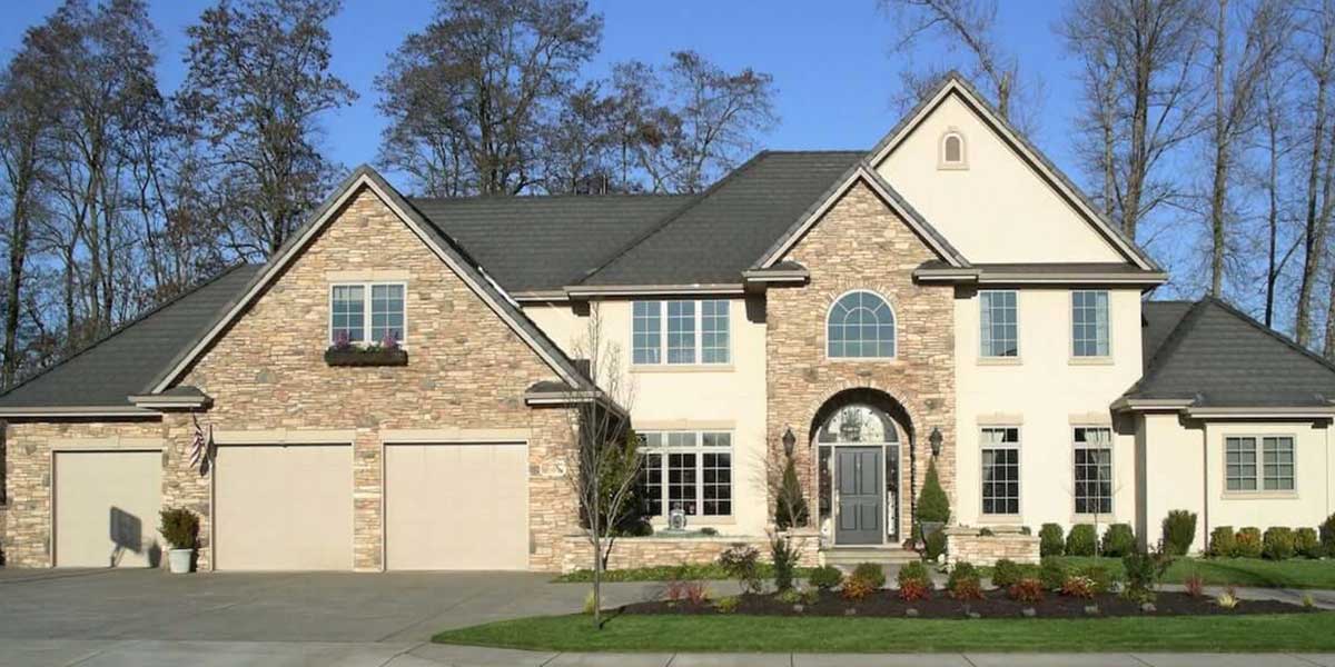 A large, modern custom home featuring stone siding, multiple garage doors, and a manicured lawn under a clear blue sky.